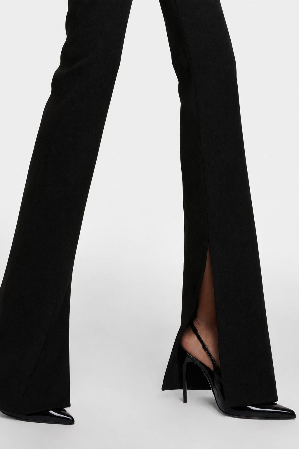 The Saint 54 black flared trousers with inner seam slits and high-waisted silhouette worn with black slingback heels