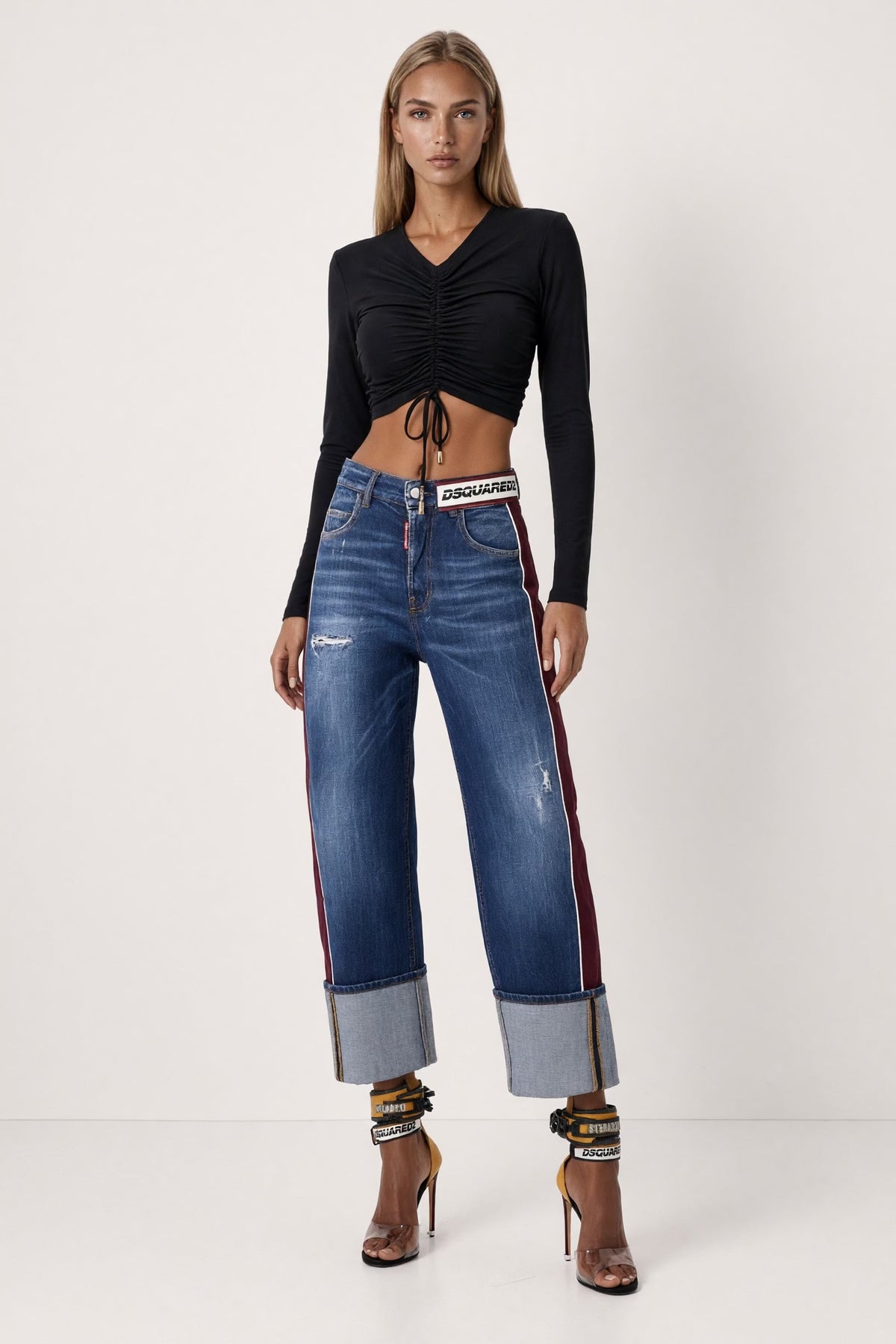 The Saint 54 black long-sleeve crop top with shoulder pads, adjustable front ties, and gold-tone tips on a model.
