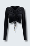The Saint 54 black long-sleeve crop top with adjustable front ruching, shoulder pads, and gold-tone tie tips.