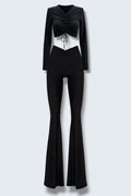 The Saint 54 black two-piece set featuring a long-sleeve ruched crop top and high-waisted flared trousers with slits.