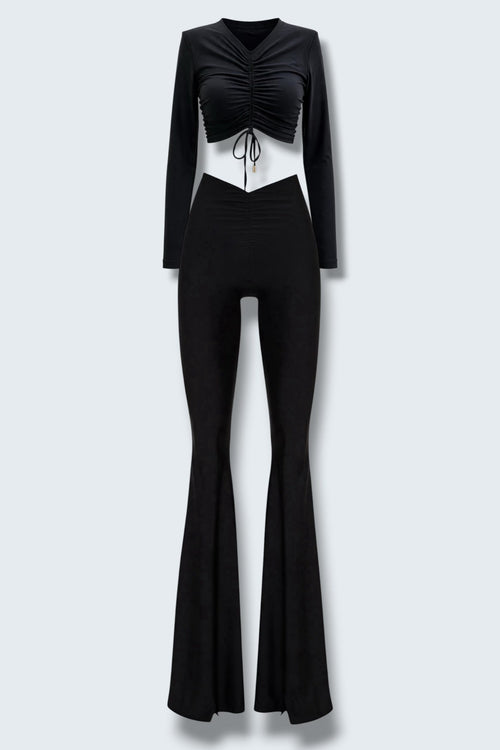 The Saint 54 black two-piece set featuring a long-sleeve ruched crop top and high-waisted flared trousers with slits.
