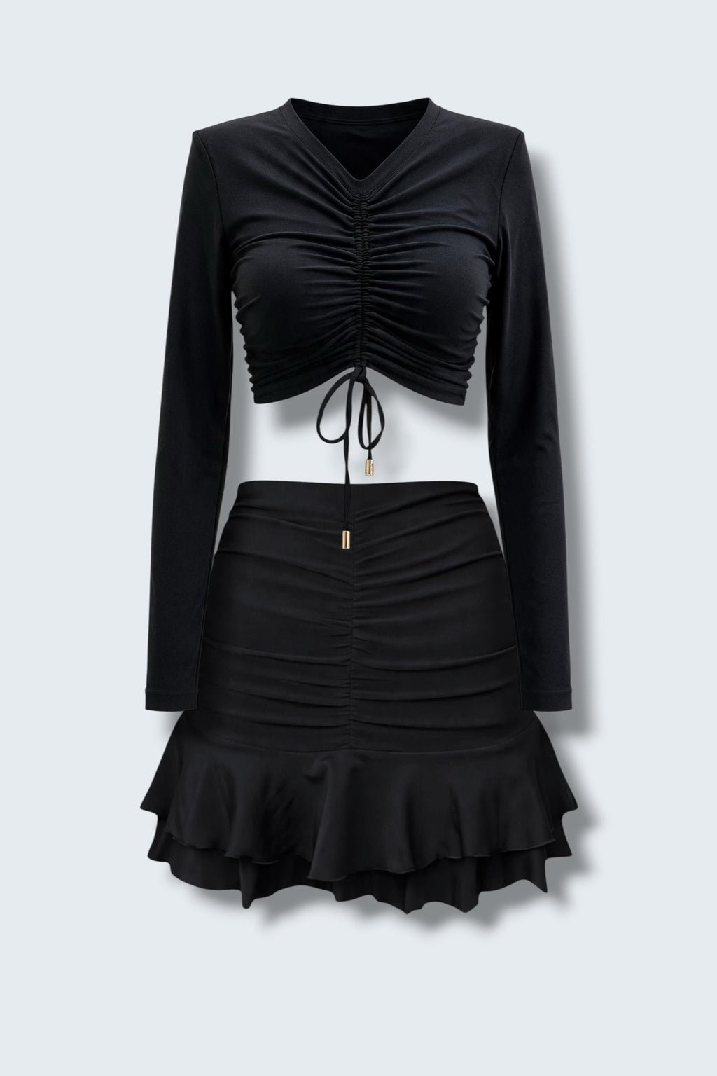 The Saint 54 black two-piece set featuring a long-sleeve ruched crop top and a matching mini skirt with ruffled hem.