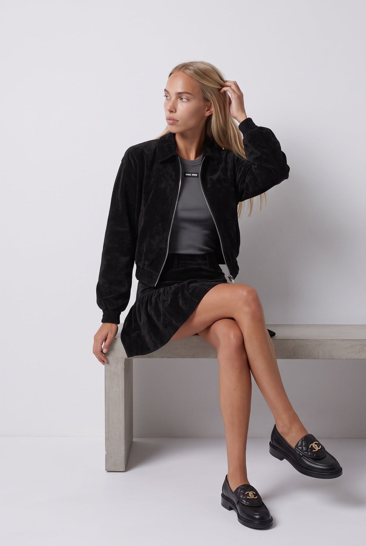 The Saint 54 black suede bomber jacket and ruffled mini skirt set worn by a model against a white background.