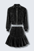 The Saint 54 black suede bomber jacket and ruffled mini skirt set worn by a model against a white background.