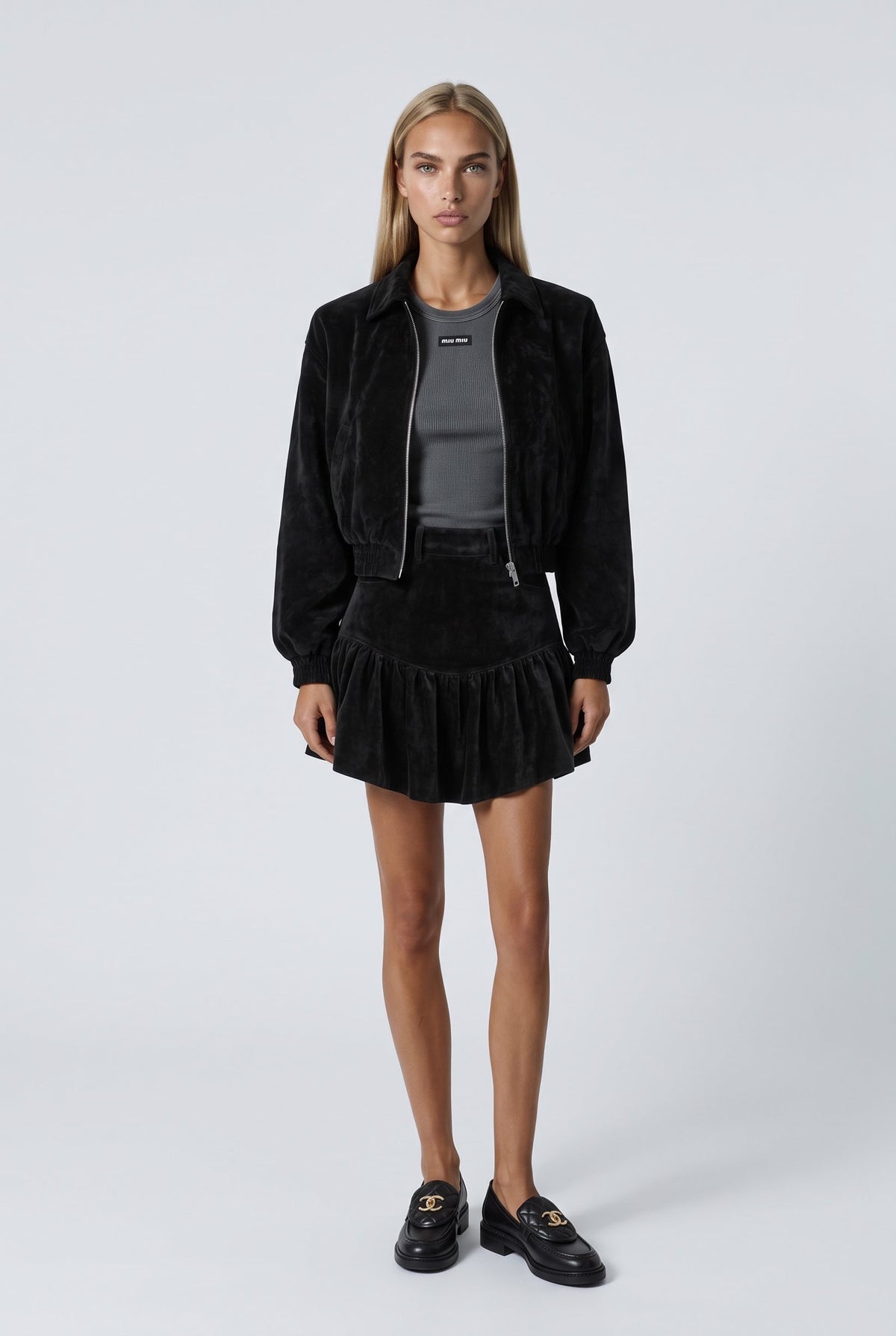 The Saint 54 black suede bomber jacket and ruffled mini skirt set worn by a model against a white background.