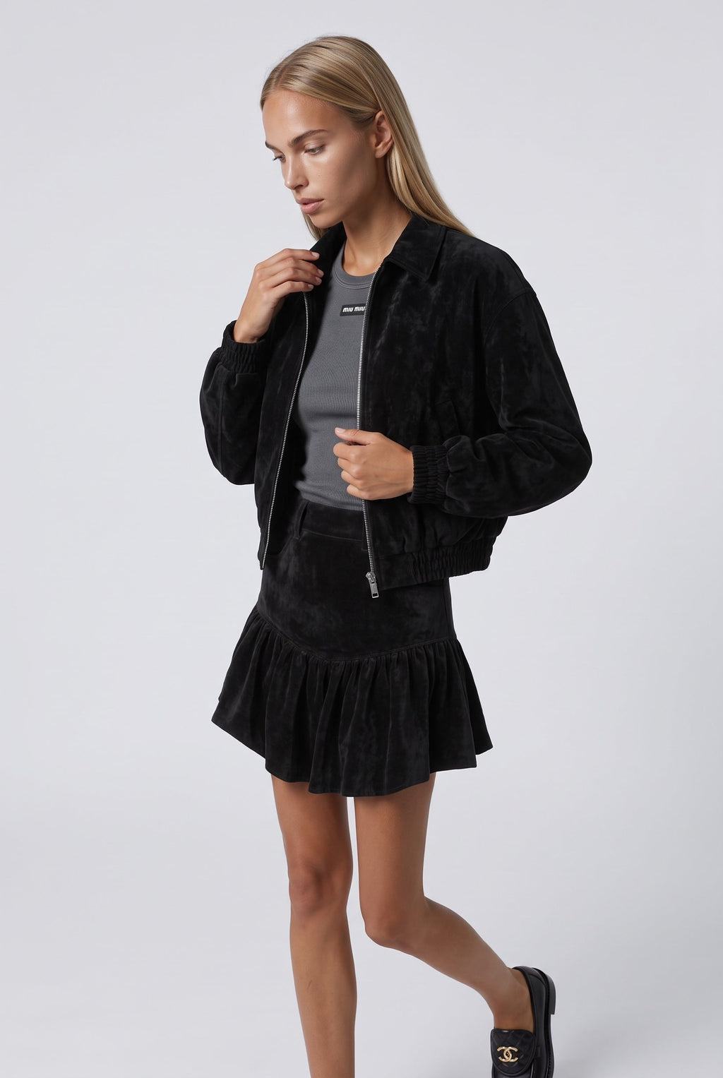 The Saint 54 black suede bomber jacket and ruffled mini skirt set worn by a model against a white background.
