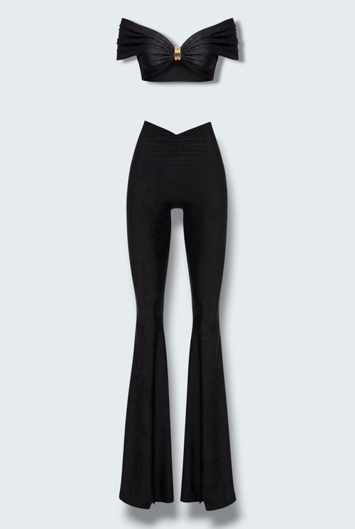 The Saint 54 black two-piece set featuring a cropped off-shoulder top with gold hardware and flared high-waisted pants.