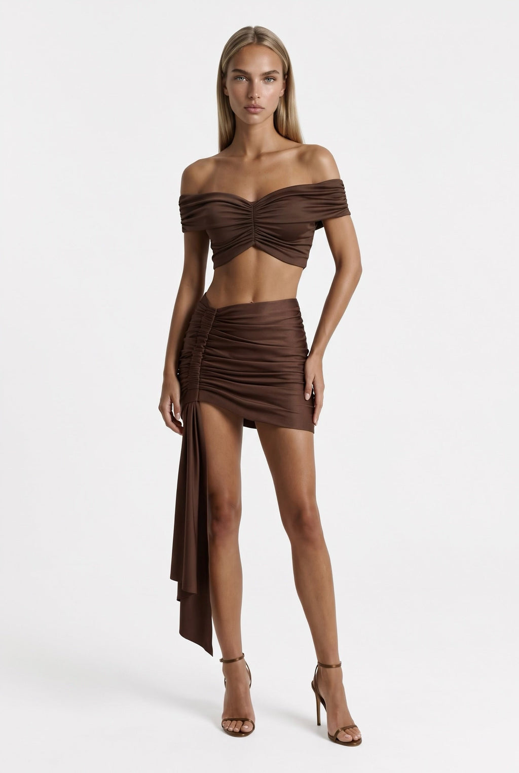 Model wearing The Saint 54 brown two-piece set with off-shoulder cropped top and ruched mini skirt with side scarf