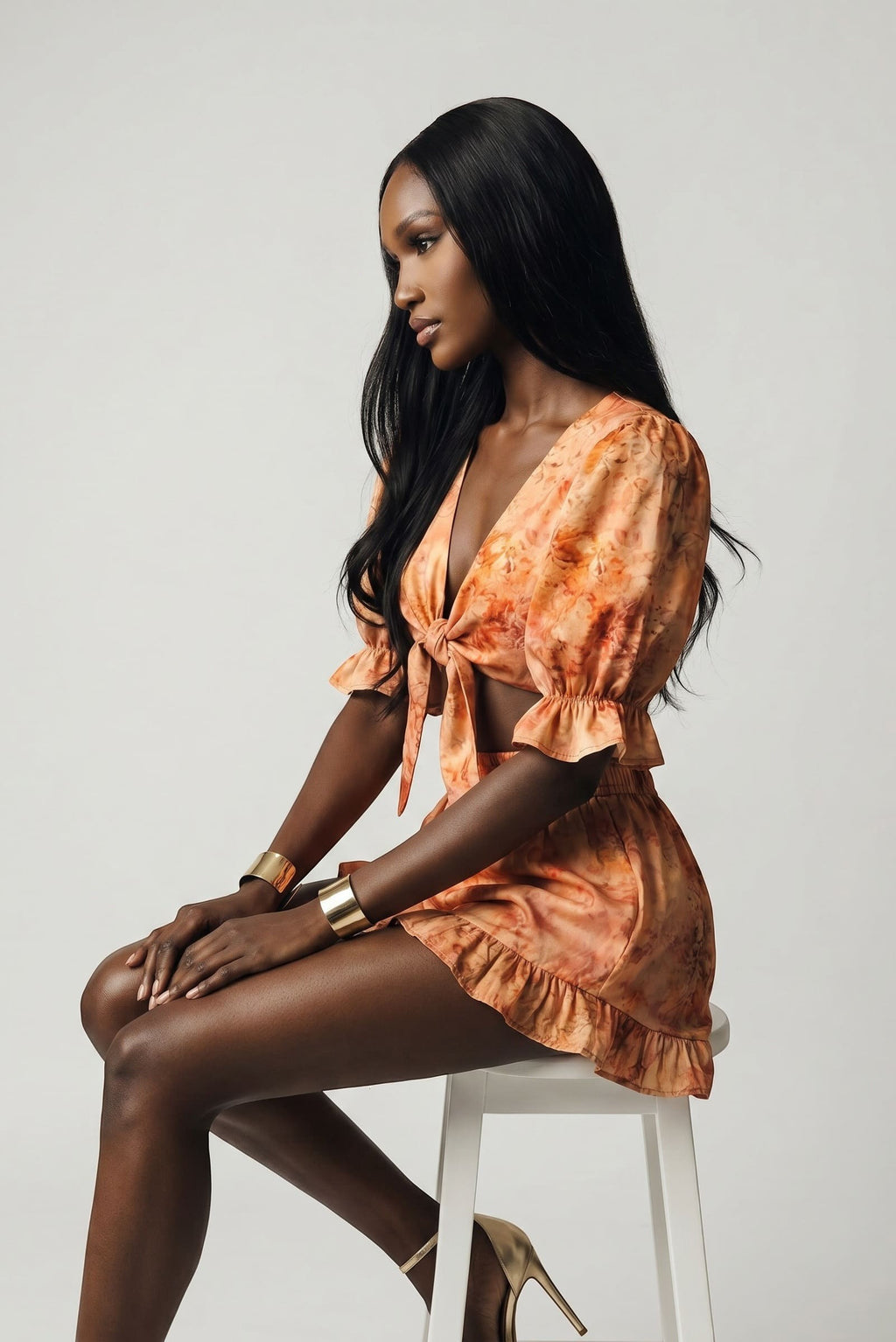 Model wearing The Saint 54 orange tie-front puff sleeve top and ruffled mini shorts set in a studio setting.