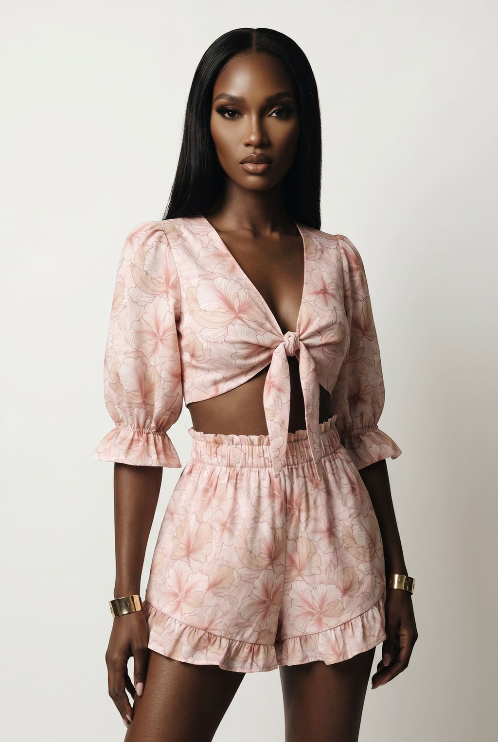 Model wearing The Saint 54 pink floral two-piece set with tie-front puff sleeve top and ruffled high-waisted shorts.